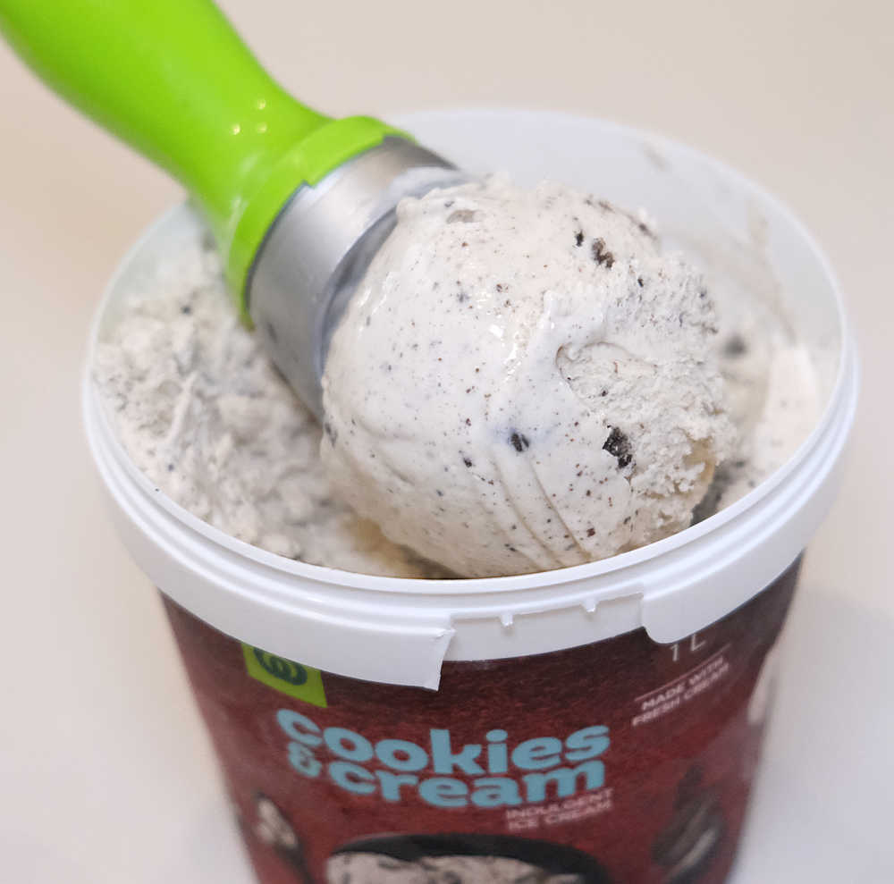 Closeup of a scoop of Woolworths Cookies and Cream Ice Cream leaning on the top of the tub.