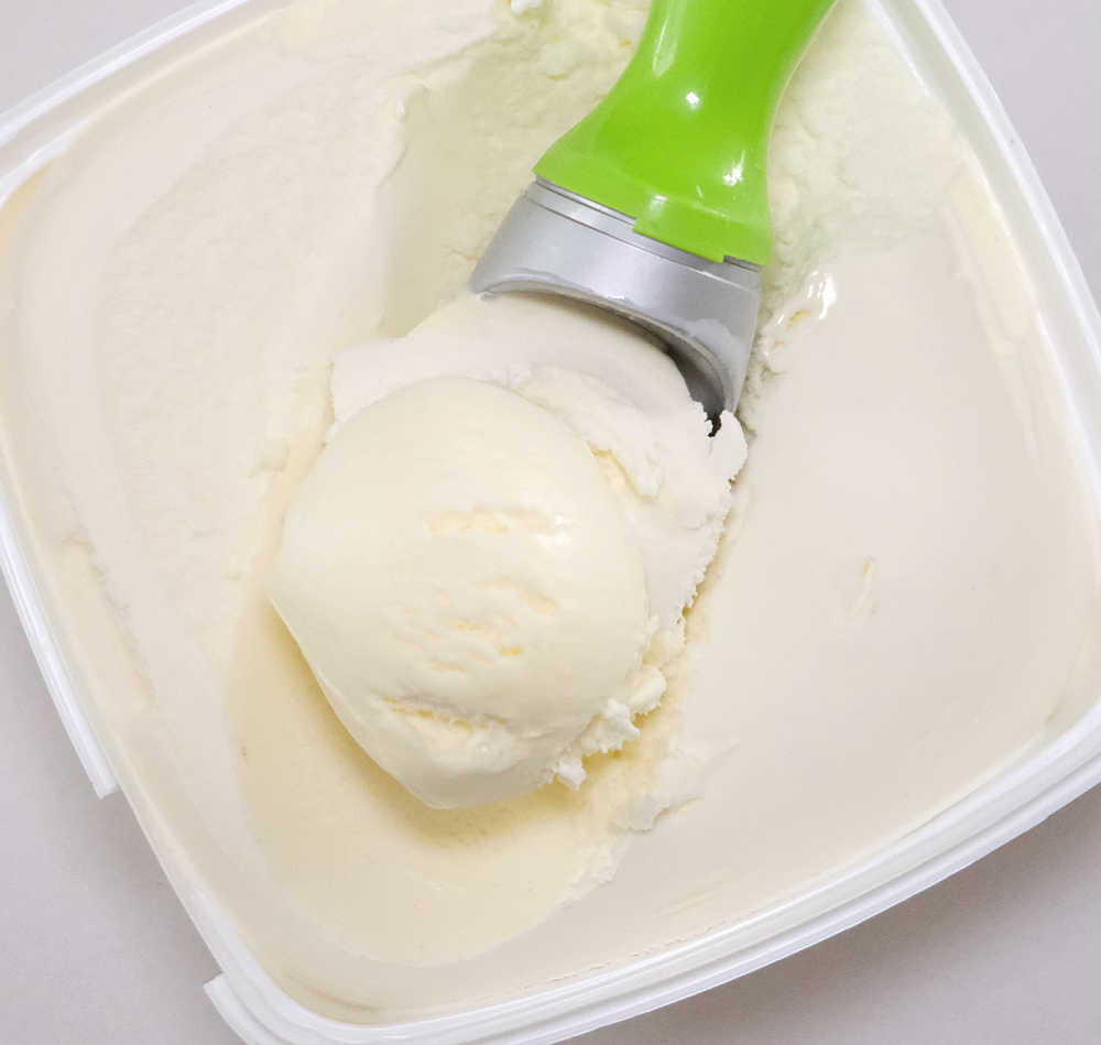 A scoop of Woolworths Vanilla Ice Cream resting on the top of the container.
