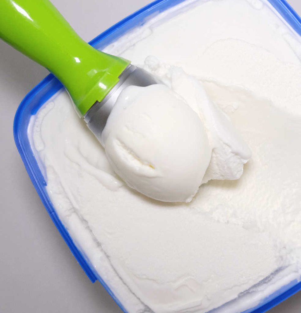 A scoop of Peters Vanilla Reduced Fat Ice Cream leaning on the pack.