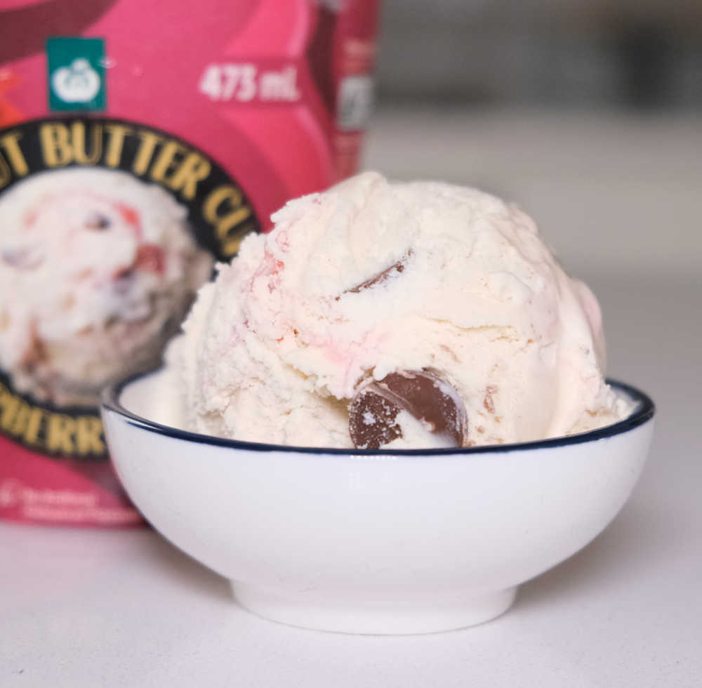 A bowl filled with Peanut Butter Cup Raspberry Ripple Ice Cream with the pack in the background.