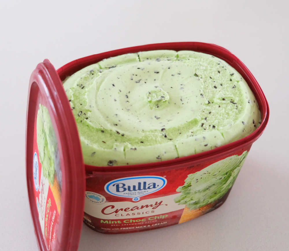 An unscooped, open container of Creamy Classics Mint Choc Chip Ice Cream.