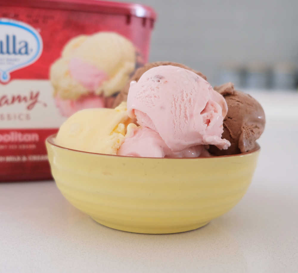 A bowl of Bulla Creamy Classics Neapolitan Ice Cream with the container behind it.