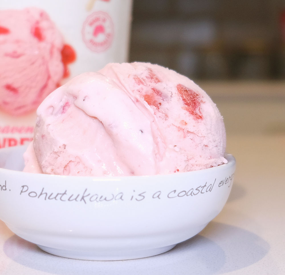 A bowl of strawberry cream ice cream with the container in the background.