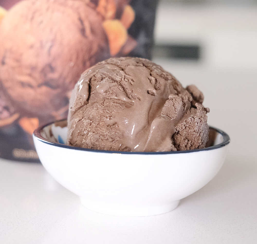 A bowl filled with a scoop of Aldi Indulge Choc Ice Cream with the container in the background.
