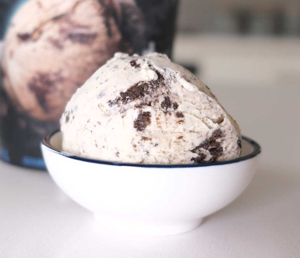 A bowl filled with Indulge Cookies and Cream Ice Cream and the container in the background.
