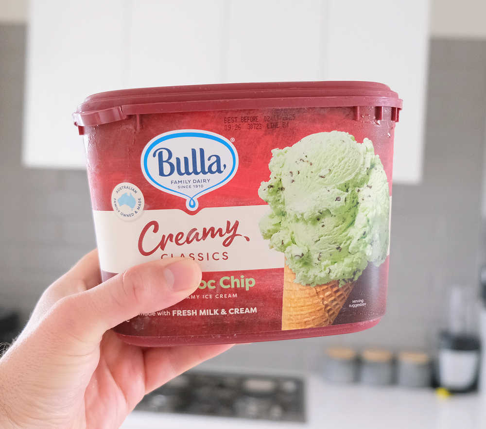 A hand holding a container of Bulla Mint Choc Chip Creamy Ice Cream.