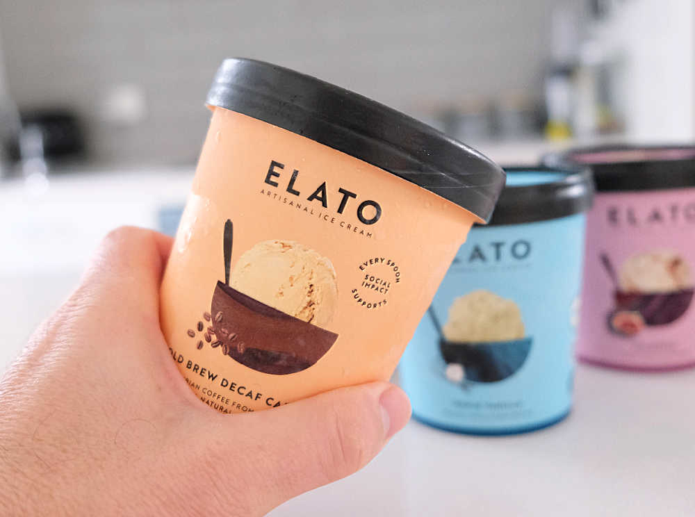 Holding a tub of Elato Cold Brew Decaf Cafe Latte Ice Cream with the rest of the range in the background.