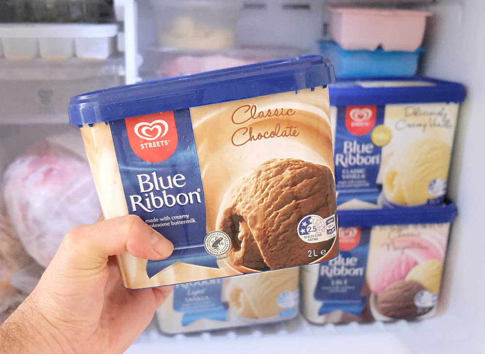 Holding a container of Blue Ribbon Classic Chocolate Ice Cream 2L in front on a home freezer.