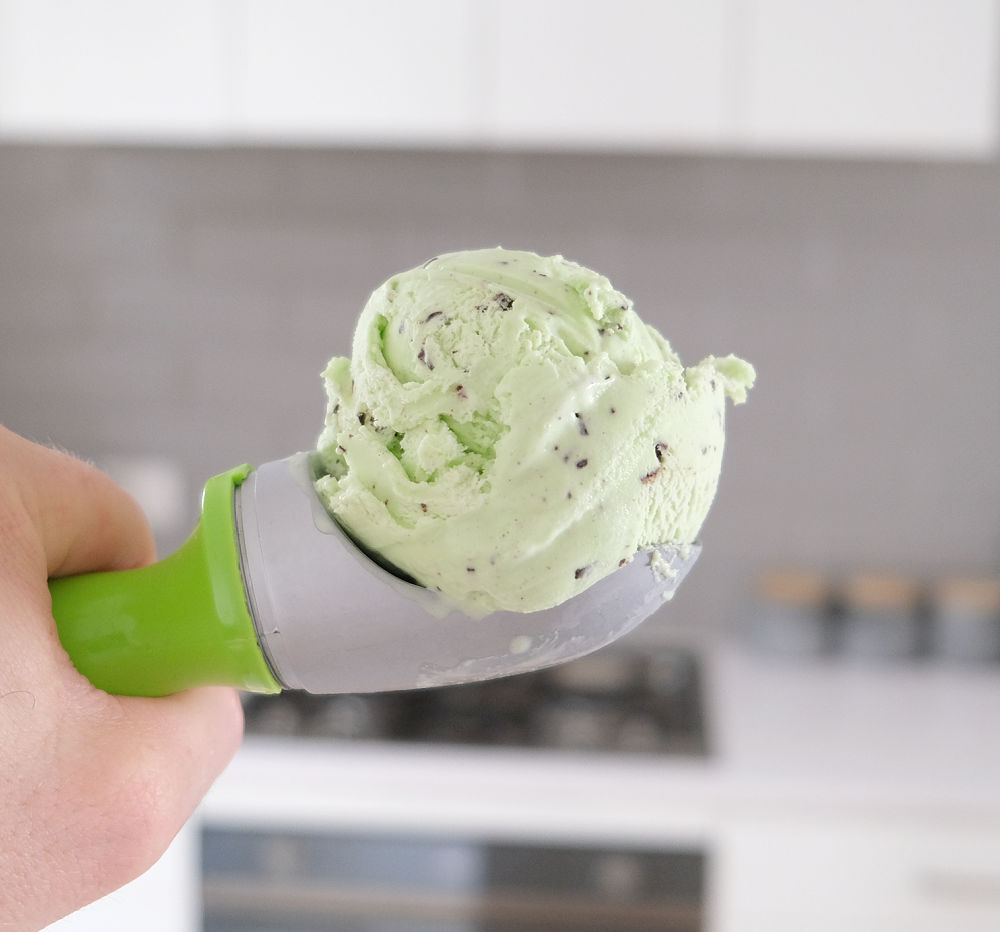 Holding a scoop of Bulla mint ice cream with a blurred kitchen in the background.