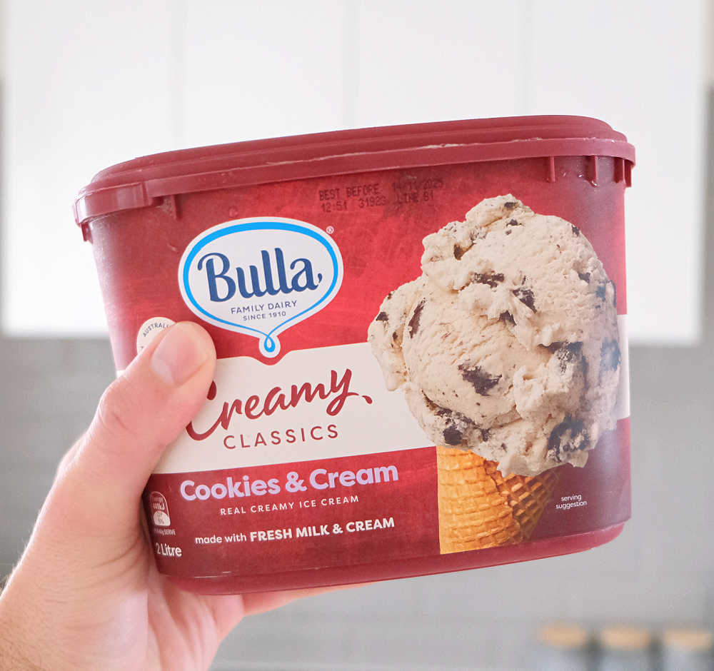 Holding a pack of Bulla Creamy Classics C&C in the kitchen.