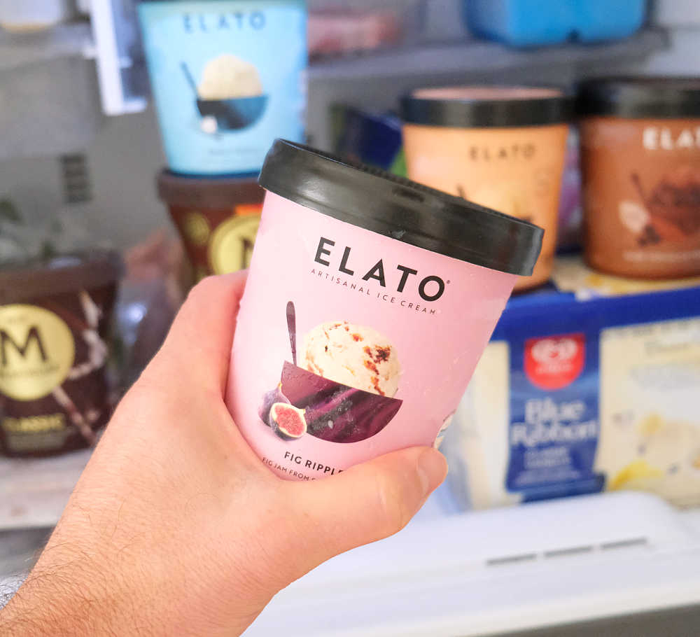 A hand holding a tub of fig ripple ice cream in front of a home freezer.