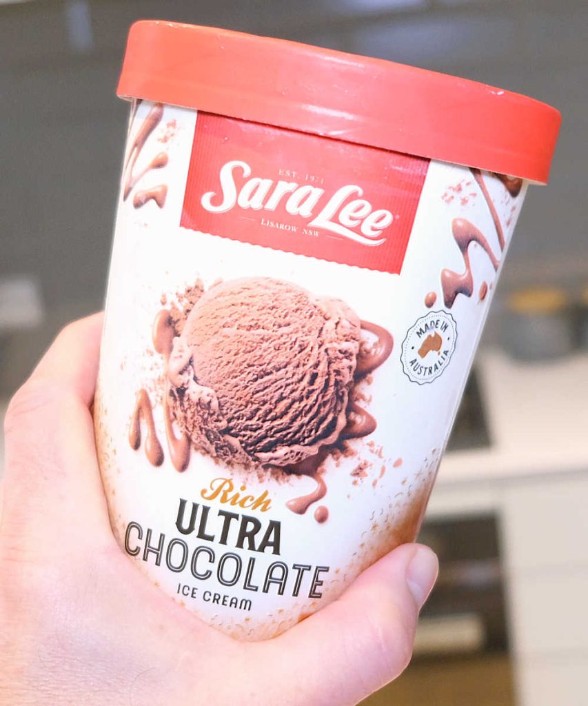 A hand holding a container of Sara Lee Chocolate Ice Cream.