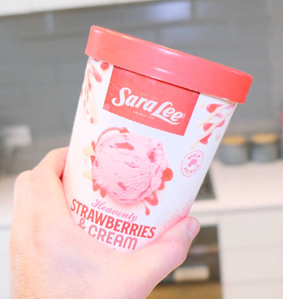 Holding a tub of Sara Lee Heavenly Strawberries and Cream Ice Cream.