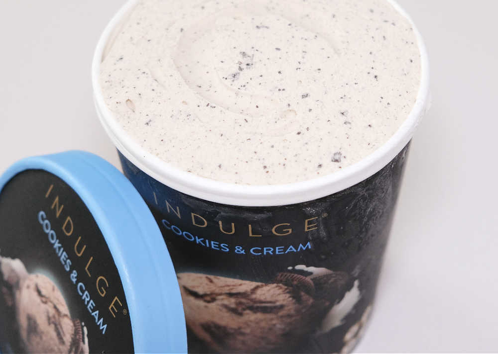 An open tub of Indulge Cookies & Cream with the lid resting against the side.