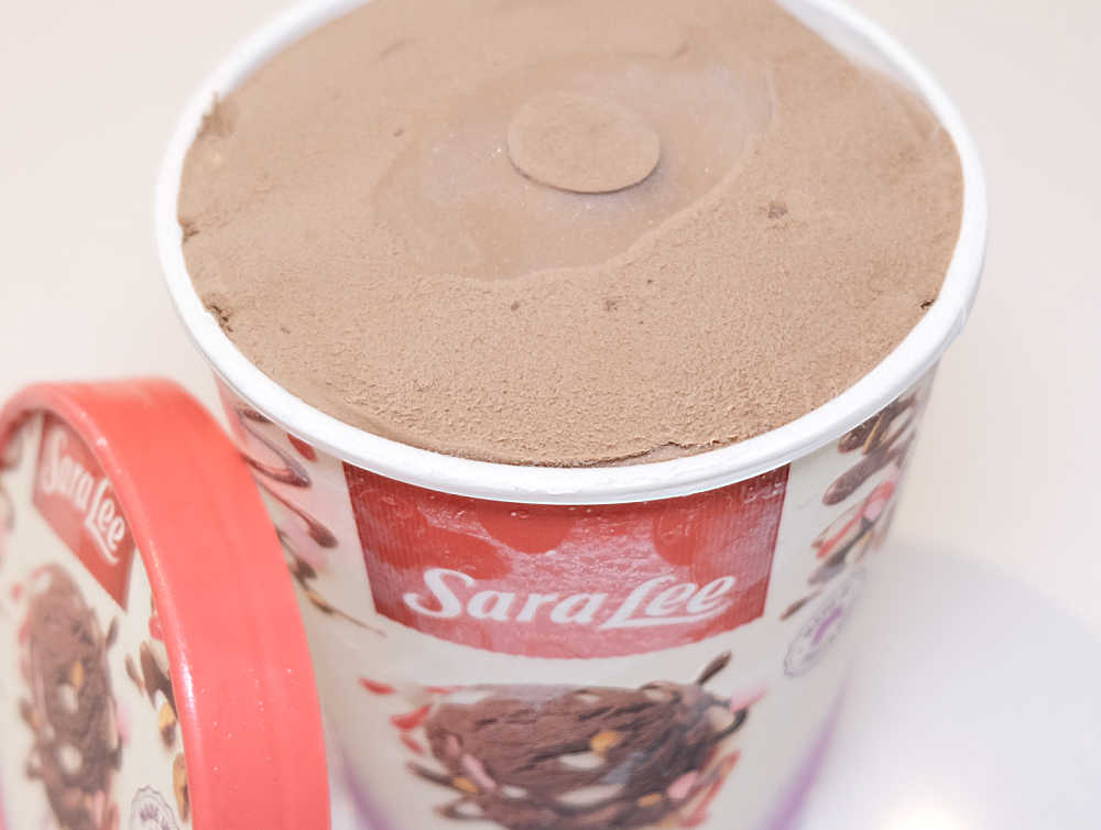 Open tub of Sara Lee Rocy Road Ice Cream with the lid resting next to the tub.