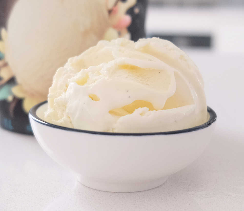A bowl of Indulge Vanilla Bean Ice Cream with the container in the background.