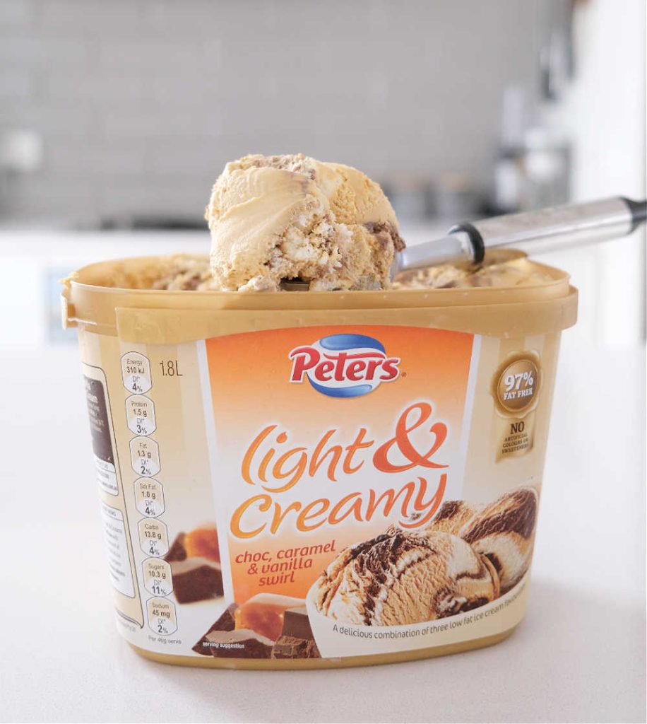 A scoop of Peters Light and Creamy Choc, Caramel and Vanilla Swirl resting on the top of the container.