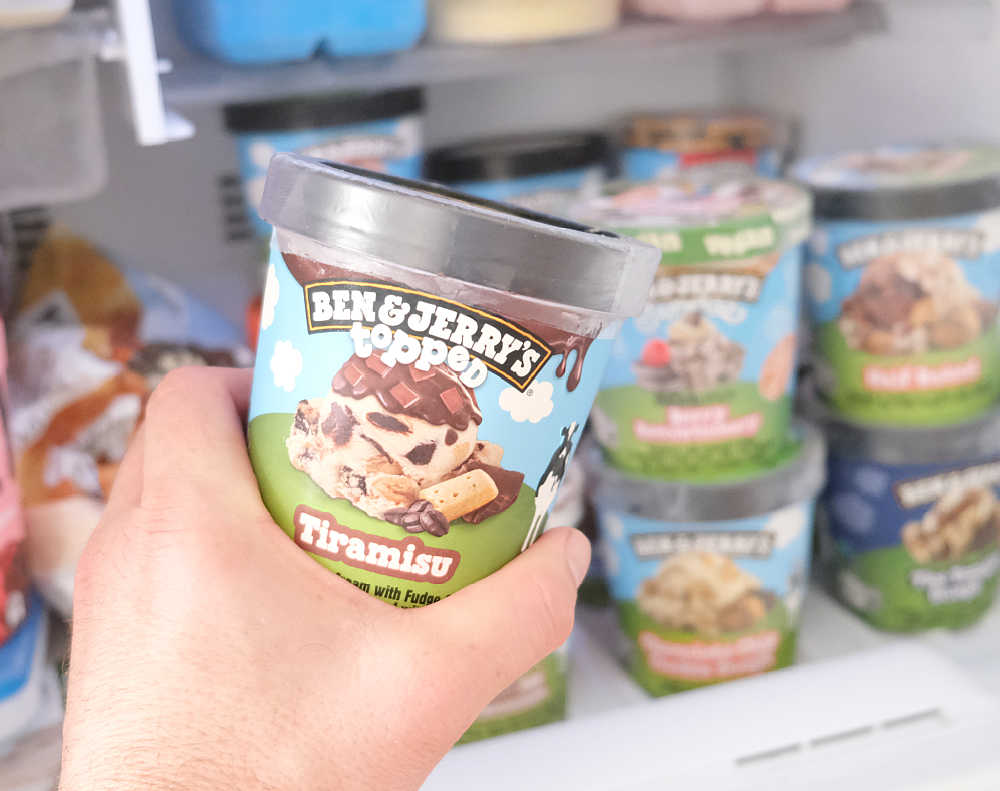 Holding a pack of Ben & Jerry's Topped Tiramisu Ice Cream in front of a home freezer.