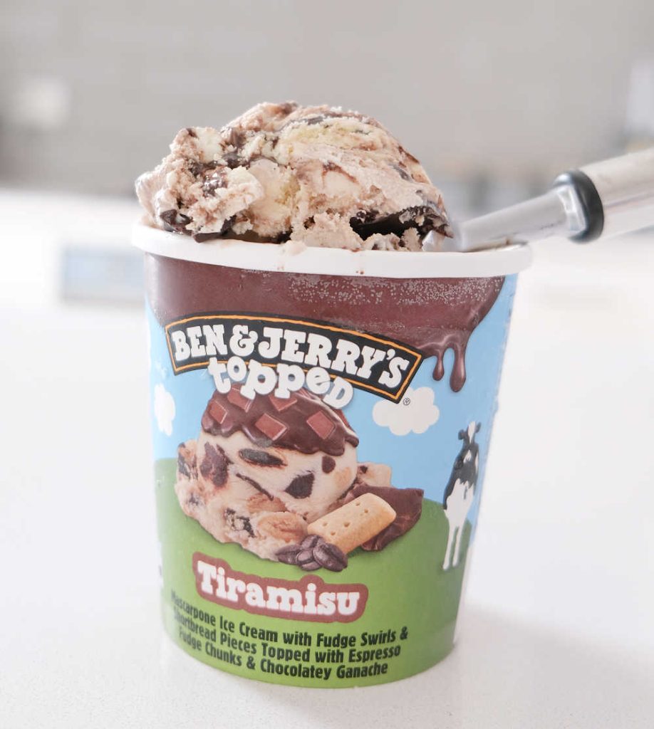 A scoop of Ben & Jerry's Topped Tiramisu Ice Cream resting on the top of the container.