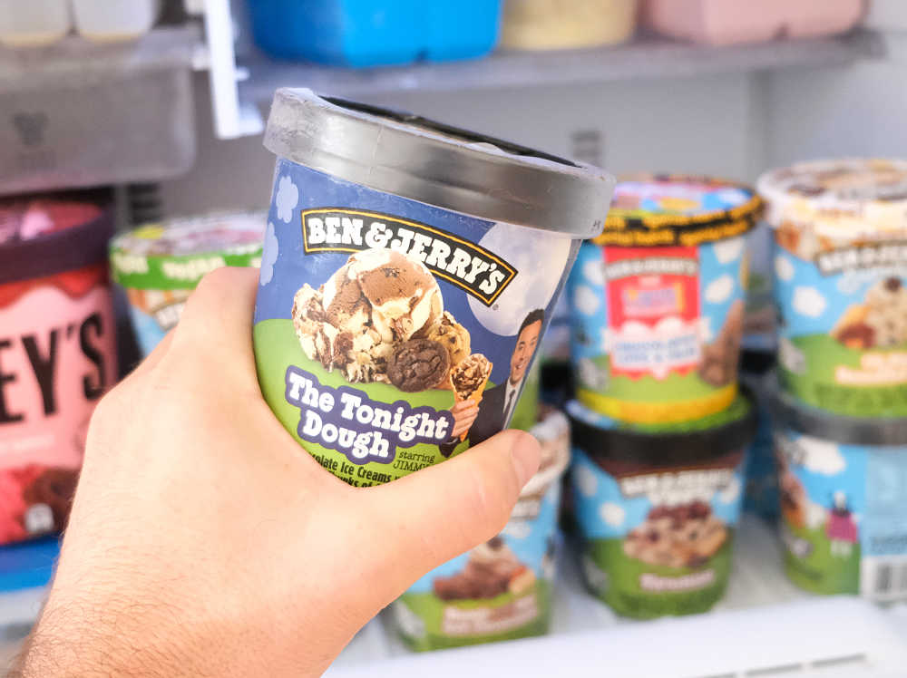 Holding a container of Ben & Jerry's The Tonight Dough with a home freezer in the background.