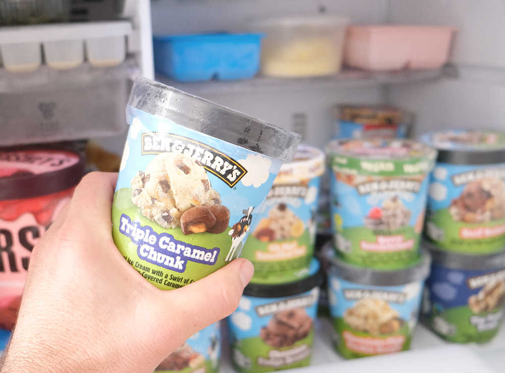 Holding a container of Ben & Jerry's Triple Caramel Chunk with a home freezer in the background.