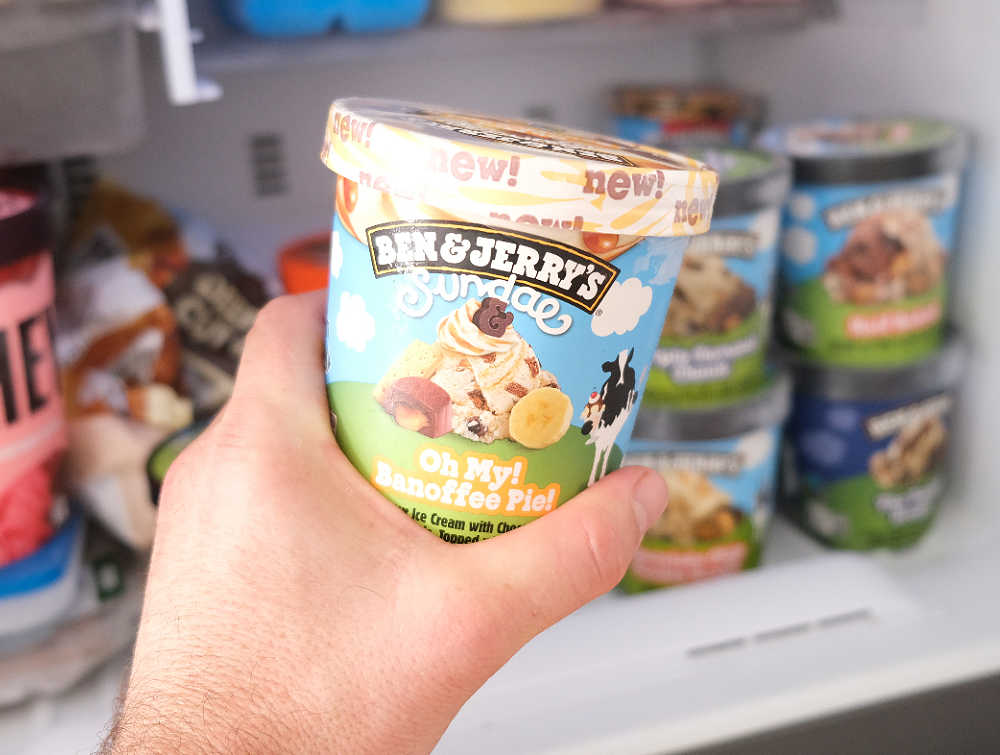 Holding a pint of Ben & Jerry's Oh My Banoffee Pie Ice Cream with a freezer in the background.