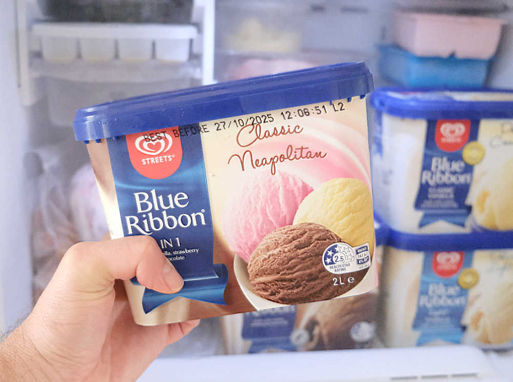 A hand holding a container of Classic Neapolitan 3-in-one.