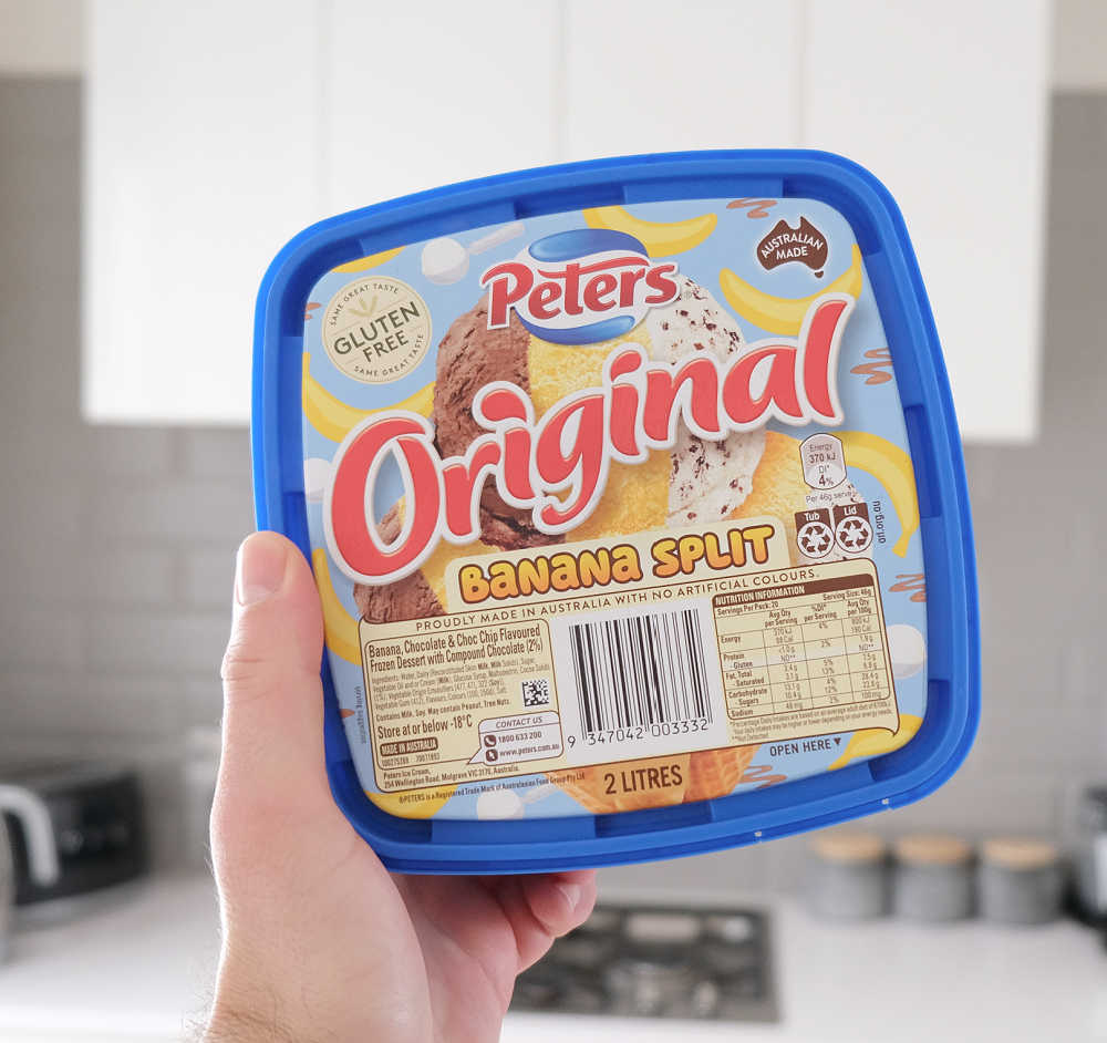 Holding a container of Peters Banana Split with a kitchen in the background.