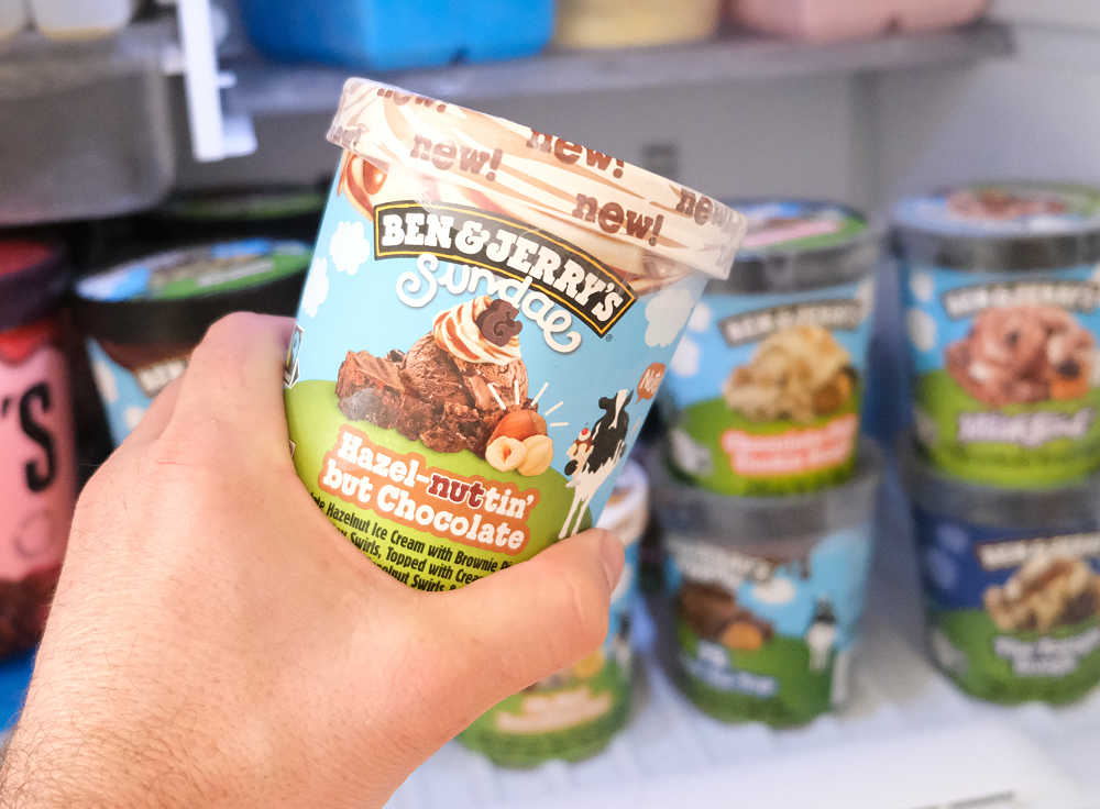 Holding a container of Ben & Jerry's Hazel-nuttin' but Chocolate Ice Cream with a home freezer in the background.