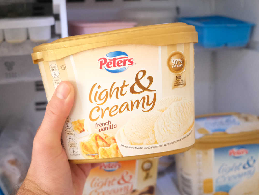 Holding a tub of Peters Light & Creamy French Vanilla 1.8L.