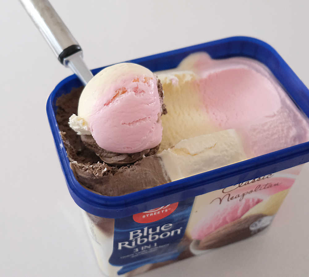 A scoop of Neapolitan Ice Cream sitting on the top of a container of Blue Ribbon.