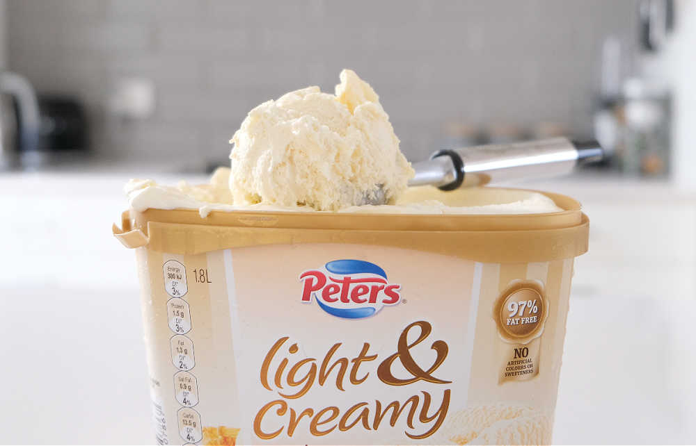 A scoop of Peters Light & Creamy French Vanilla resting on the top of the container.