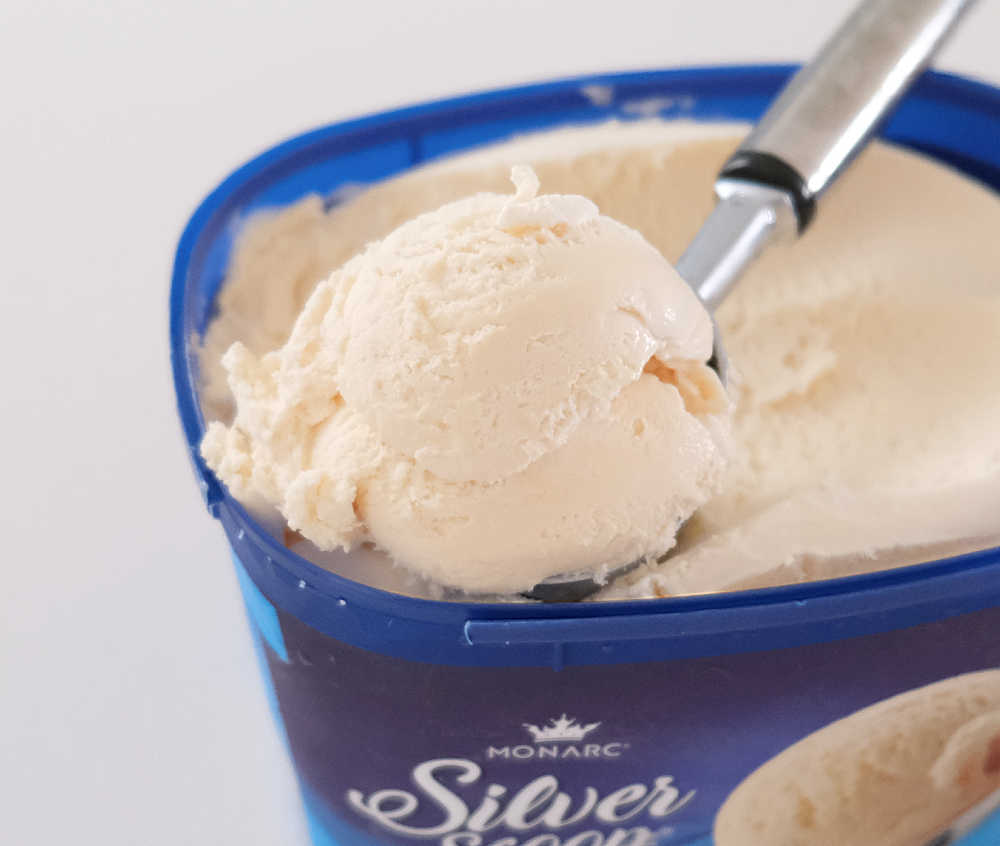 Closeup of a scoop of Silver Scoop Vanilla Ice Cream resting on the top of the tub.