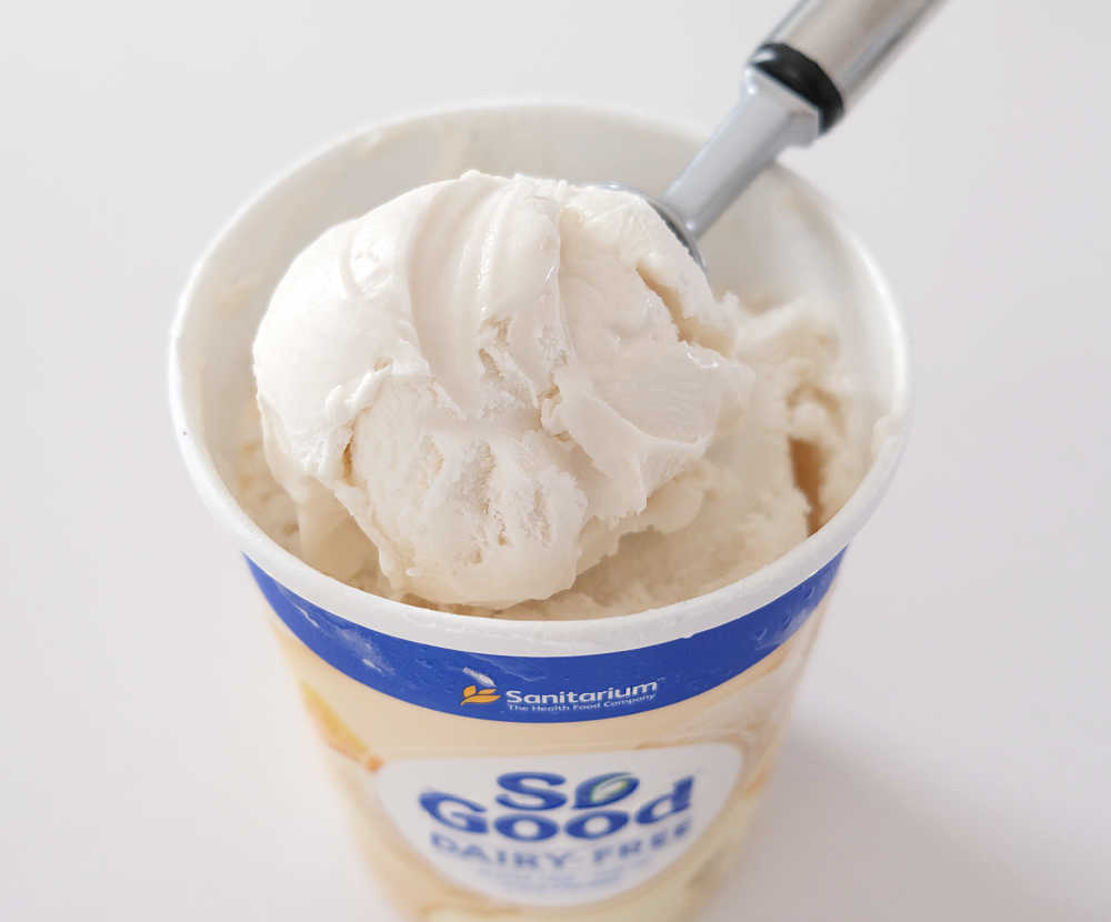 A scoop of So Good Vanilla Frozen Dessert resting on the tub.
