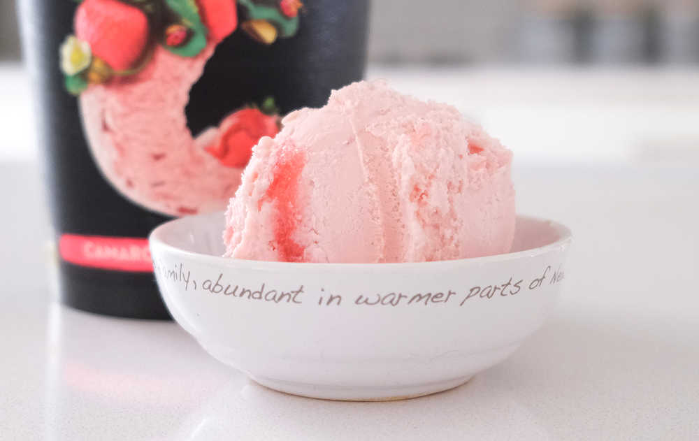 A bowl of Connoisseur Ice Cream Camarosa Strawberry with the packaging in the background.
