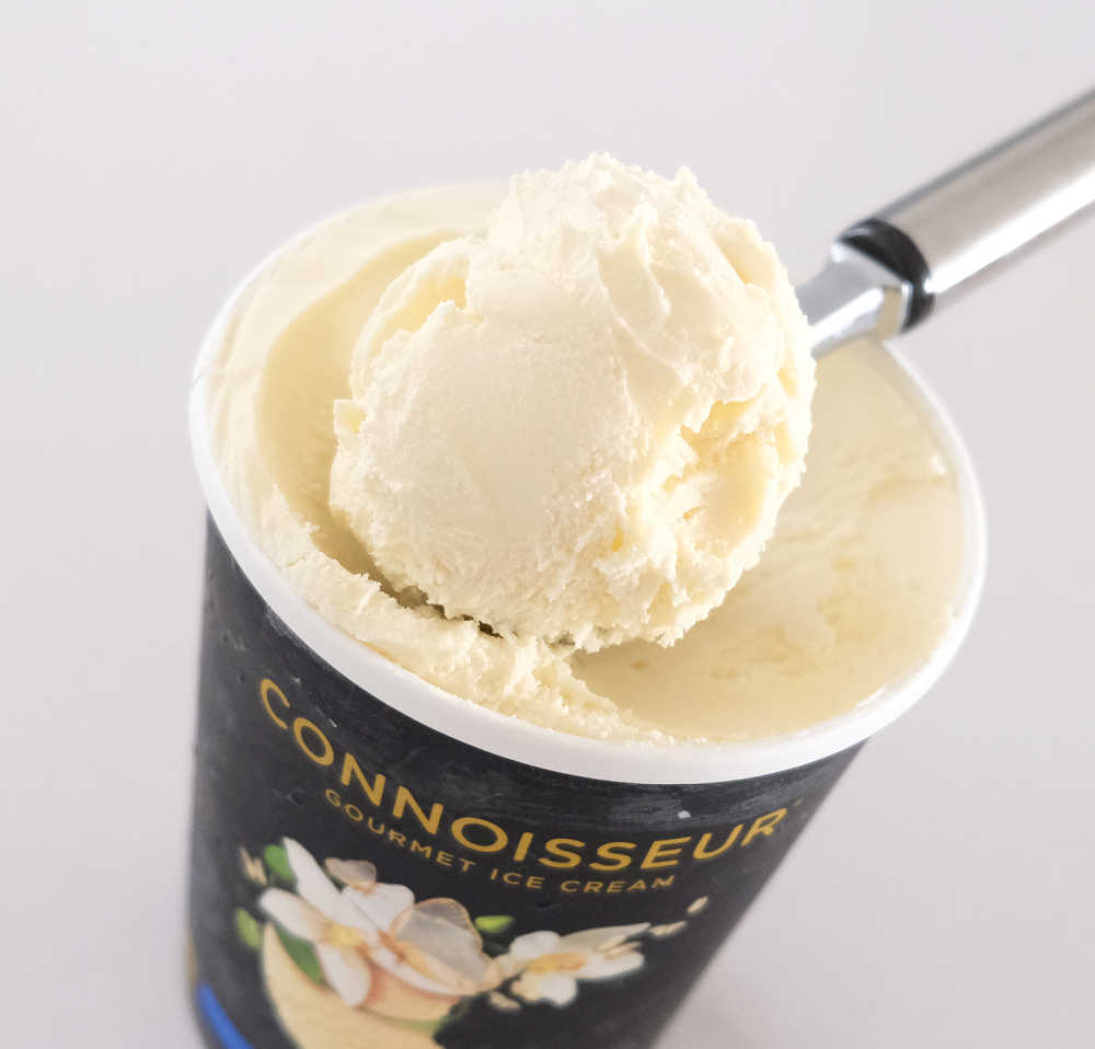 A closeup photo of a scoop of Connoisseur Gourmet Vanilla Ice Cream resting on the top of the container.