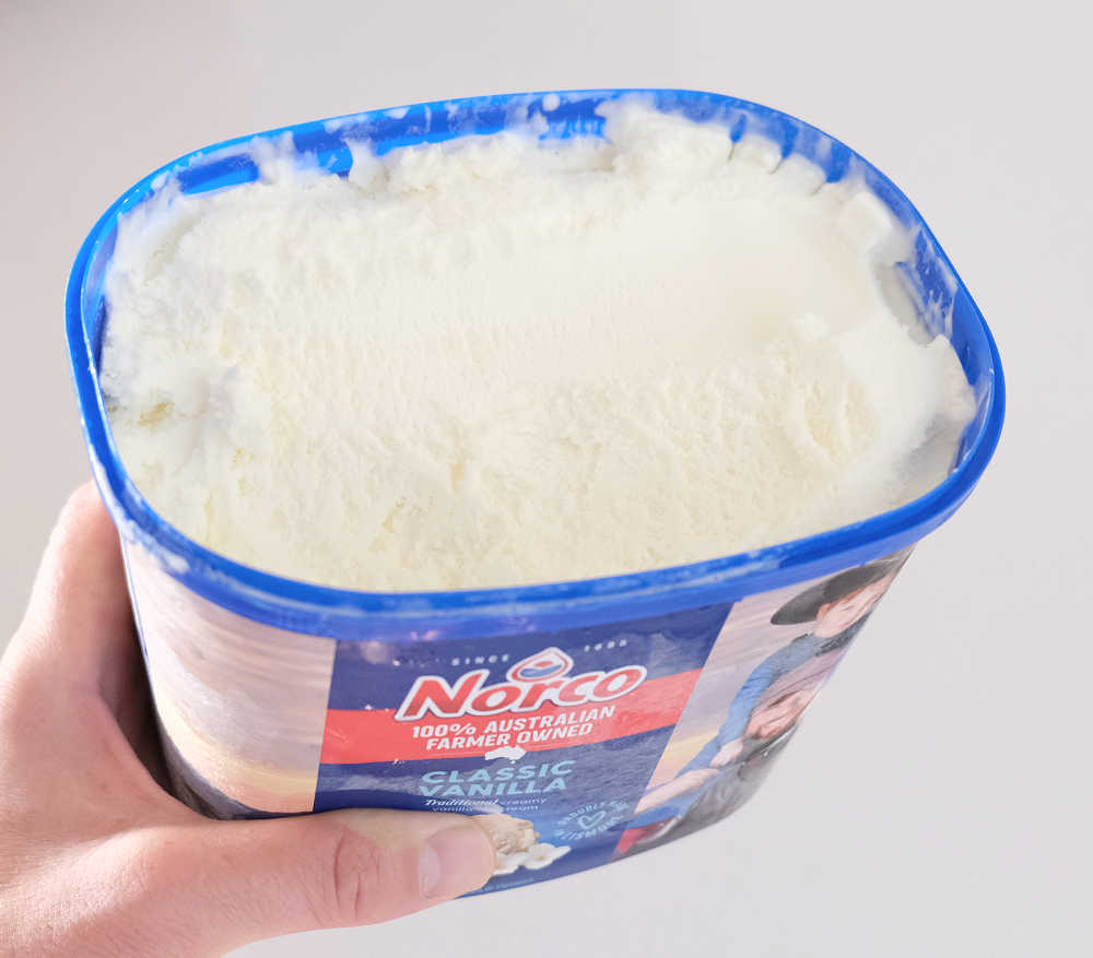Holding an opened container of Norco Classic Vanilla Ice Cream.