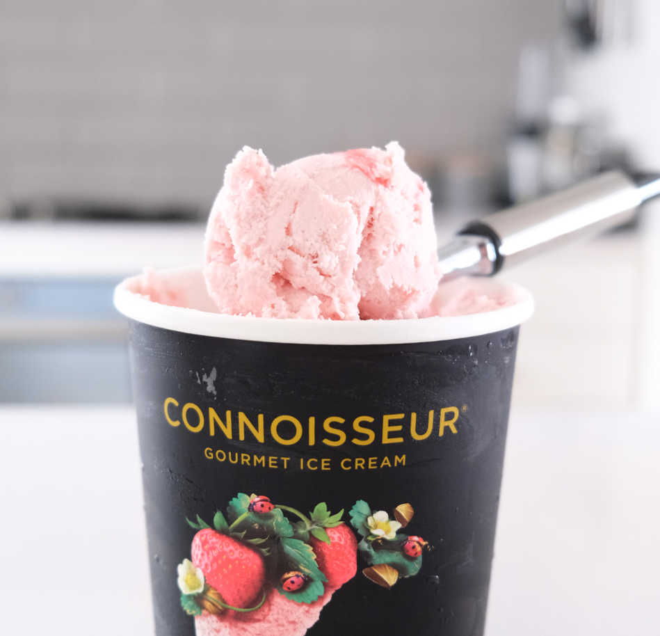 A scoop of Connoisseur Strawberry Ice Cream resting on the top of the container.