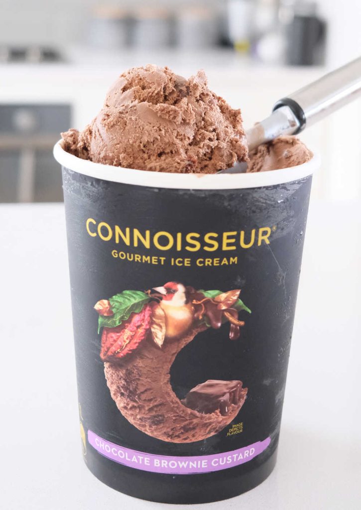 A vertical photo of a scoop of Connoisseur Chocolate Brownie Custard Ice Cream resting on the container.