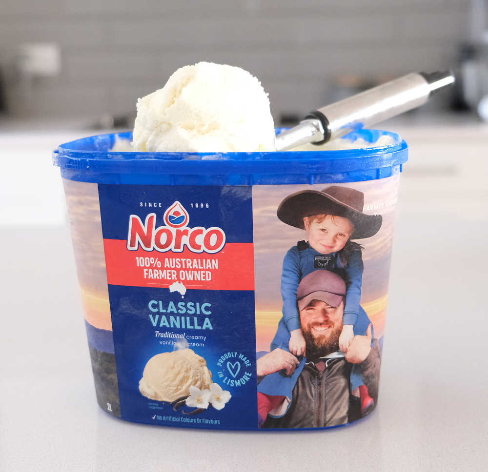 A scoop of Norco Classic Vanilla Ice Cream resting on the tub.