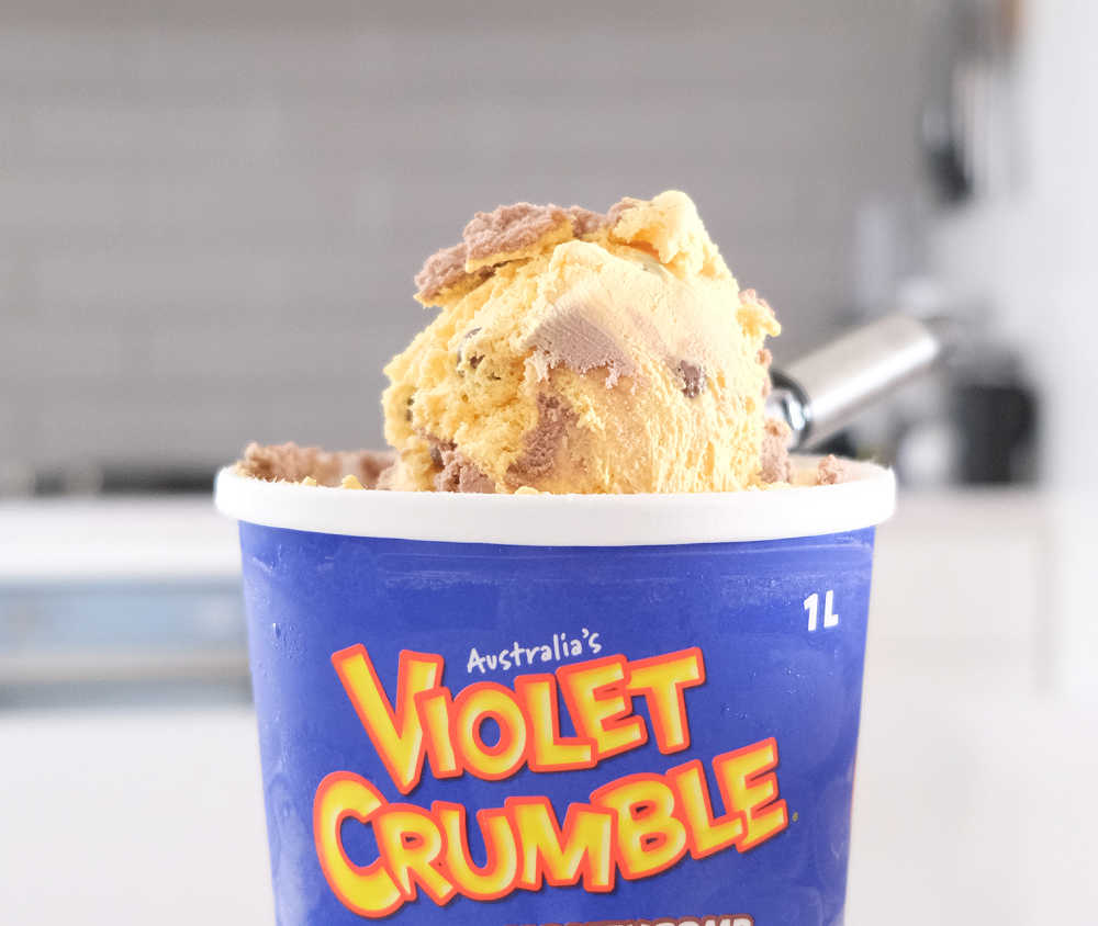 A scoop of Violet Crumble Choc Ice Cream resting on the top of the container.