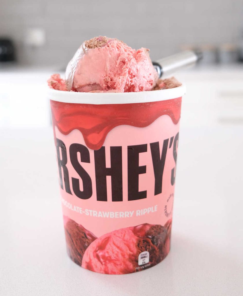 A tub of Hershey's Chocolate-Strawberry Ripple Ice Cream 1L on a kitchen bench.
