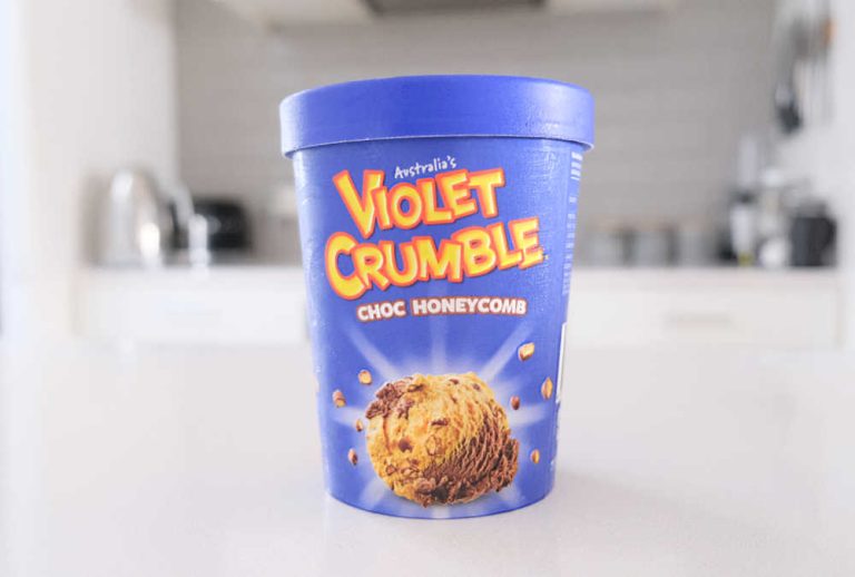A tub of Violet Crumble Choc Honeycomb Ice Cream sitting on a kitchen bench.
